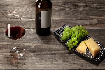 Image showing A bottle and a glass of red wine with fruits over wooden background