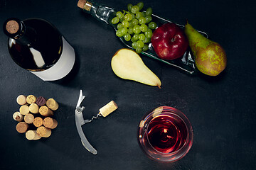 Image showing A bottle and a glass of red wine with fruits over dark stone background