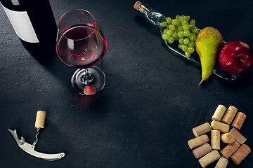 Image showing A bottle and a glass of red wine with fruits over dark stone background