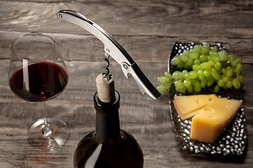 Image showing A bottle and a glass of red wine with fruits over wooden background