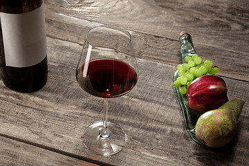 Image showing A bottle and a glass of red wine with fruits over dark stone background