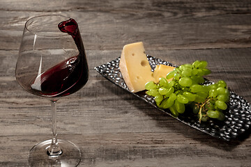 Image showing A bottle and a glass of red wine with fruits over wooden background