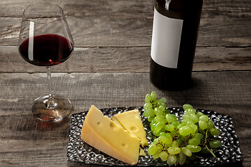 Image showing A bottle and a glass of red wine with fruits over wooden background