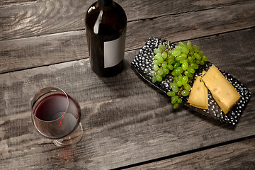 Image showing A bottle and a glass of red wine with fruits over wooden background