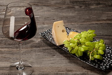Image showing A bottle and a glass of red wine with fruits over wooden background