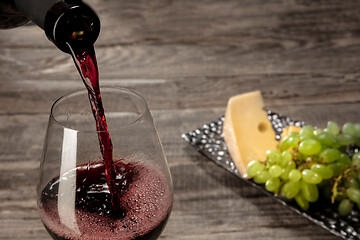 Image showing A bottle and a glass of red wine with fruits over wooden background