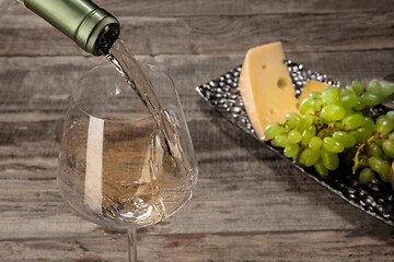 Image showing A bottle and a glass of white wine with fruits over wooden background