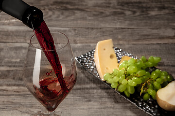 Image showing A bottle and a glass of red wine with fruits over wooden background