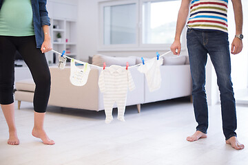 Image showing young couple holding baby bodysuits at home