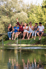 Image showing friends enjoying watermelon while sitting on the wooden bridge