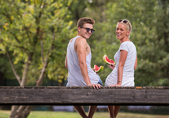 Image showing couple enjoying watermelon while sitting on the wooden bridge