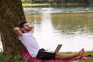 Image showing man using a laptop computer on the bank of the river