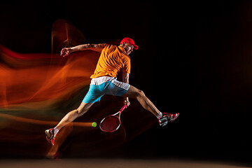 Image showing One caucasian man playing tennis on black background