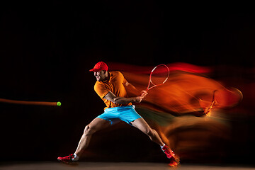 Image showing One caucasian man playing tennis on black background