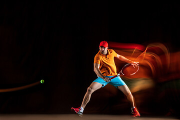 Image showing One caucasian man playing tennis on black background