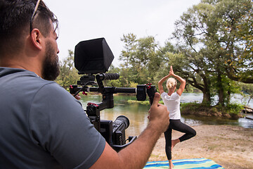 Image showing young videographer recording while woman doing yoga exercise