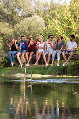 Image showing friends enjoying watermelon while sitting on the wooden bridge