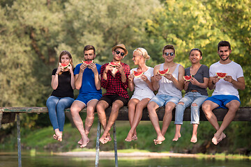 Image showing friends enjoying watermelon while sitting on the wooden bridge