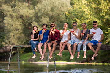 Image showing friends enjoying watermelon while sitting on the wooden bridge