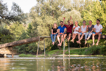 Image showing friends enjoying watermelon while sitting on the wooden bridge