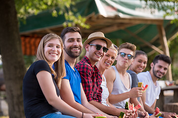 Image showing friends enjoying watermelon while sitting on the wooden bridge