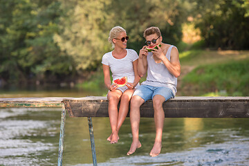 Image showing couple enjoying watermelon while sitting on the wooden bridge