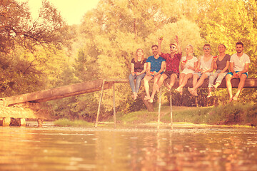 Image showing friends enjoying watermelon while sitting on the wooden bridge