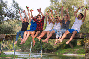 Image showing friends enjoying watermelon while sitting on the wooden bridge