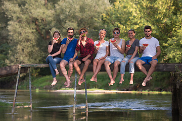 Image showing friends enjoying watermelon while sitting on the wooden bridge