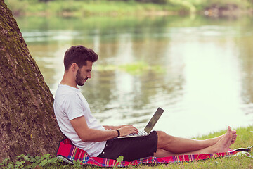 Image showing man using a laptop computer on the bank of the river