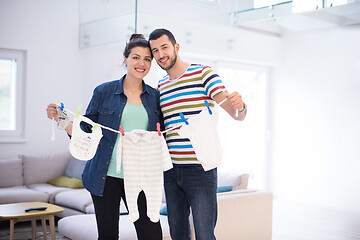 Image showing young couple holding baby bodysuits at home