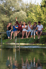 Image showing friends enjoying watermelon while sitting on the wooden bridge