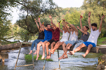 Image showing friends enjoying watermelon while sitting on the wooden bridge