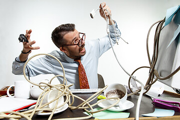 Image showing Young man tangled in wires on the workplace