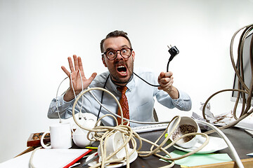 Image showing Young man tangled in wires on the workplace