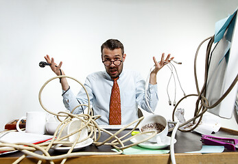 Image showing Young man tangled in wires on the workplace