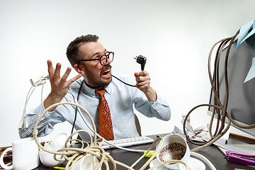 Image showing Young man tangled in wires on the workplace