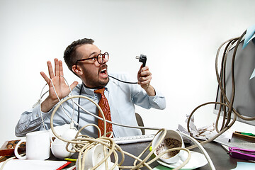 Image showing Young man tangled in wires on the workplace