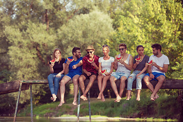 Image showing friends enjoying watermelon while sitting on the wooden bridge