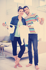 Image showing young couple holding baby bodysuits at home