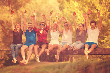 Image showing friends enjoying watermelon while sitting on the wooden bridge