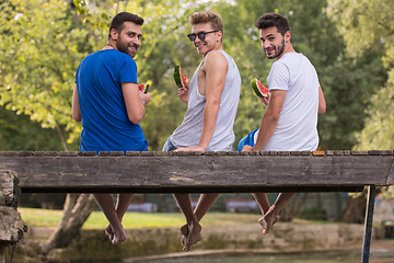 Image showing men enjoying watermelon while sitting on the wooden bridge