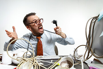 Image showing Young man tangled in wires on the workplace