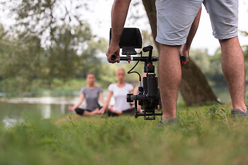 Image showing young videographer recording while woman doing yoga exercise