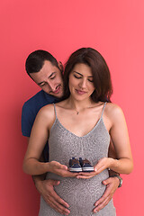 Image showing young pregnant couple holding newborn baby shoes