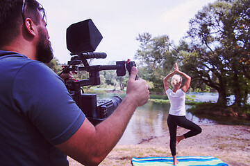 Image showing young videographer recording while woman doing yoga exercise