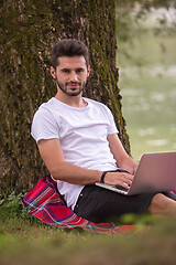 Image showing man using a laptop computer on the bank of the river