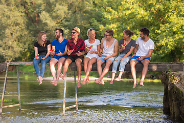 Image showing friends enjoying watermelon while sitting on the wooden bridge