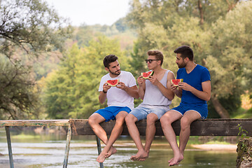 Image showing men enjoying watermelon while sitting on the wooden bridge