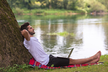 Image showing man using a laptop computer on the bank of the river